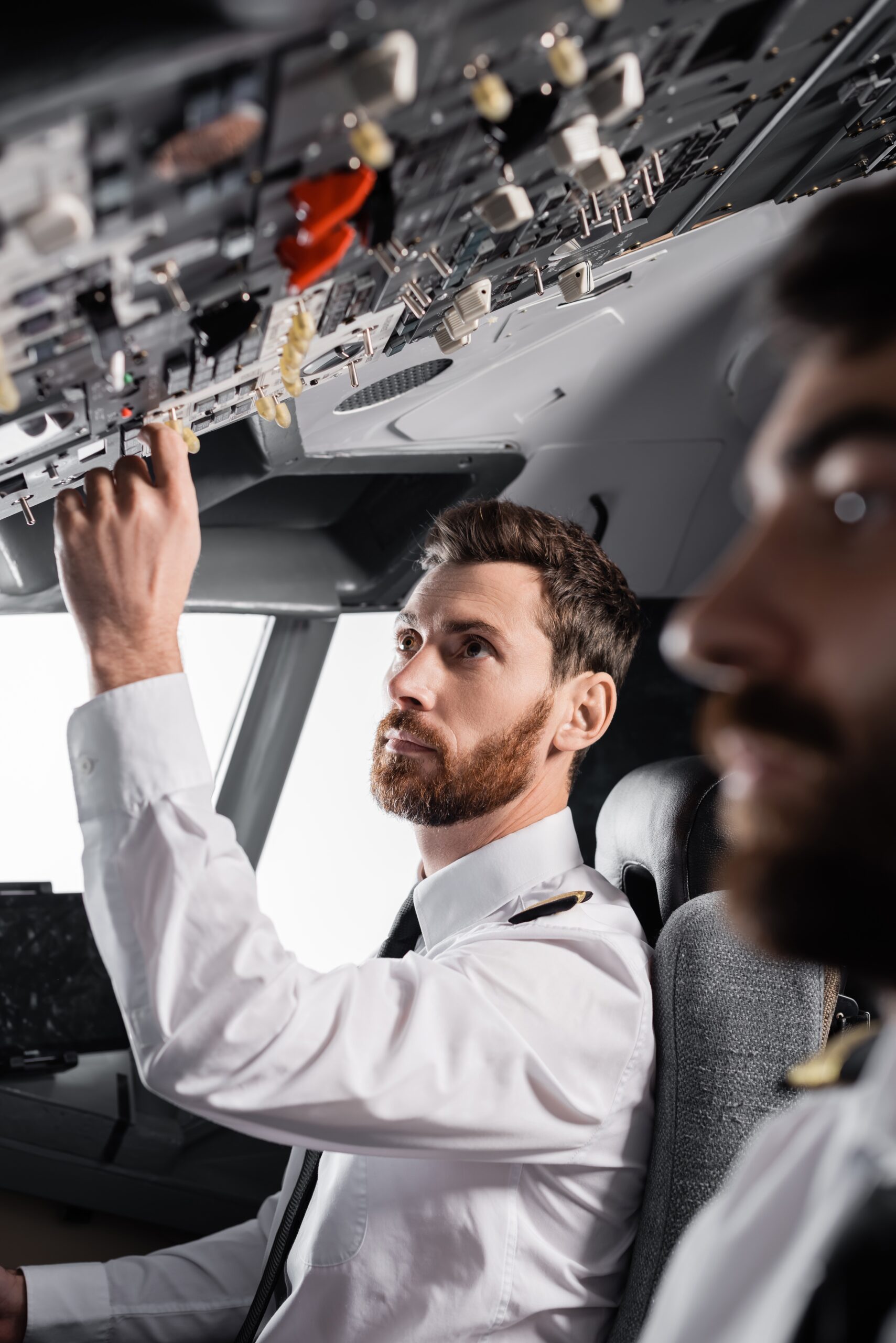 Bearded,Pilot,Reaching,Overhead,Panel,Near,Co-pilot,In,Airplane,Simulator